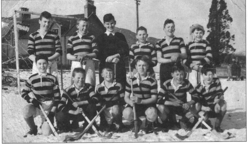 Black and white image of the Fort William Shinty team of the 1950s lined up with their shinty sticks for a group photograph