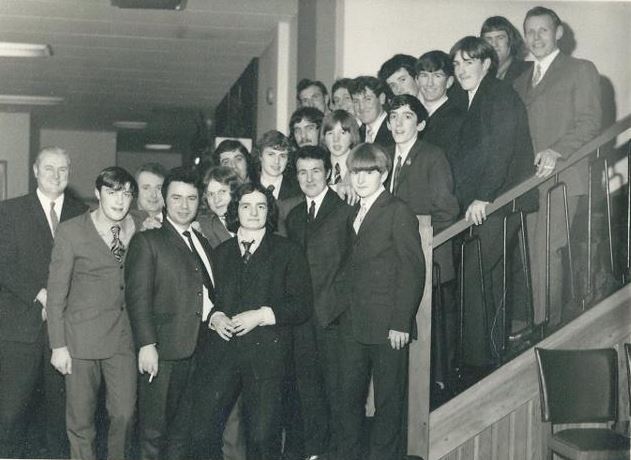 Black and white image of the Fort William team of the 1970s lined up on a staircase at a formal occasion in suits