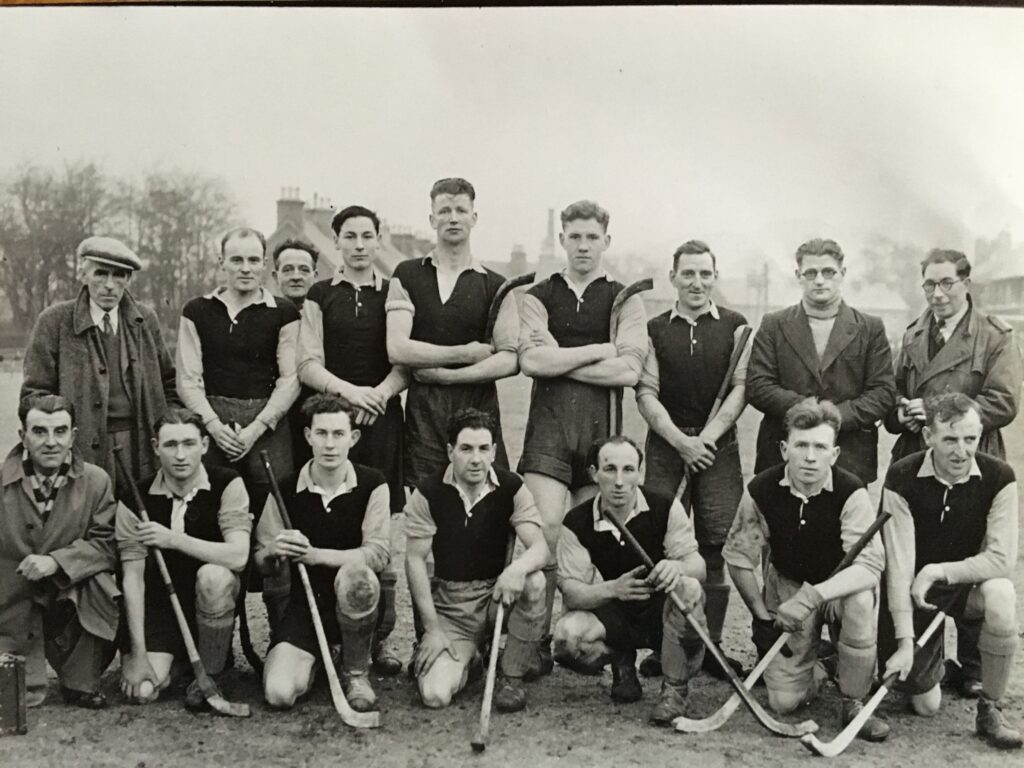 Two rows of shinty players lined up for a team photograph in 1946-47. Wearing team kit and posing with their shinty sticks