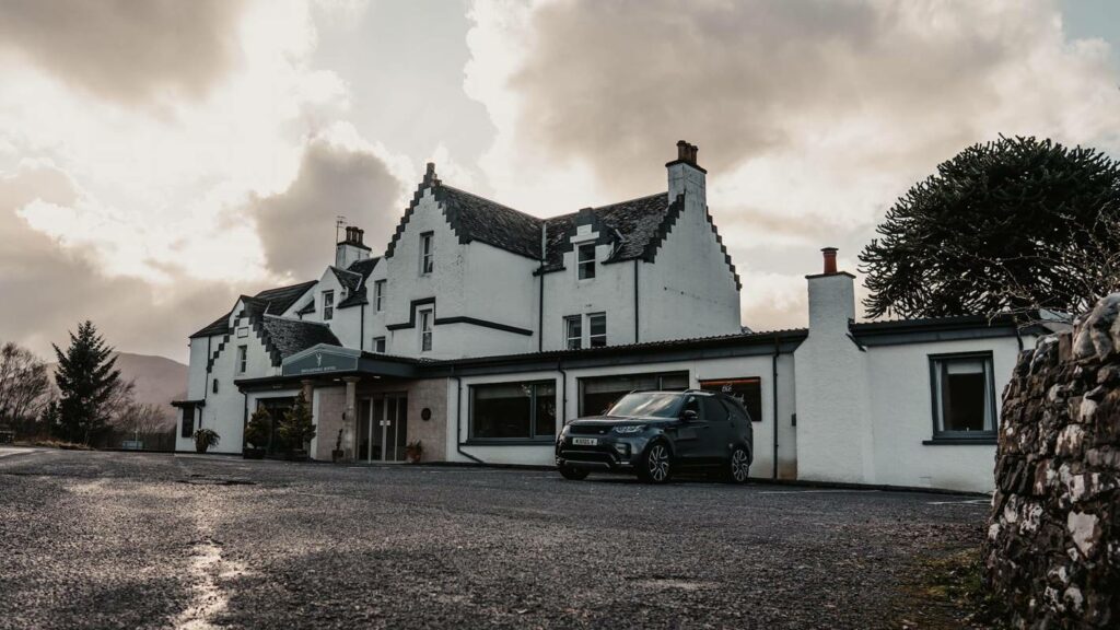 Black and white photograph of a white building painted with black window sills and a slate roof. A public house