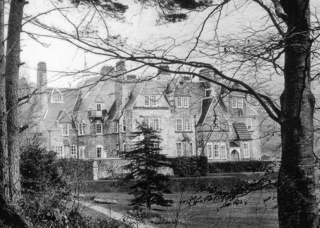 Black and white photograph of a large house with trees in the foregroudn