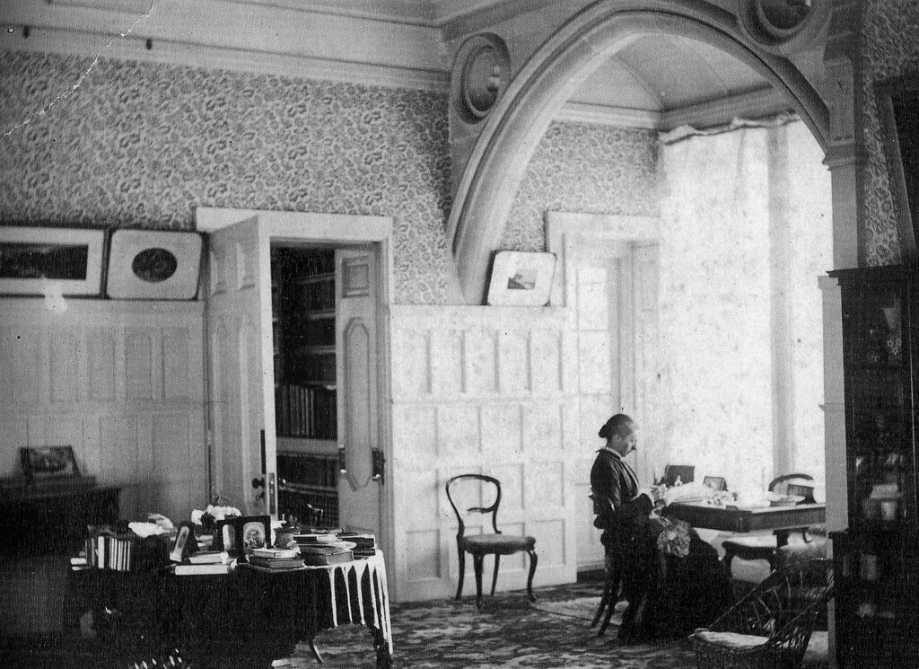 Black and white photograph of a lady sat beside a window reading a book